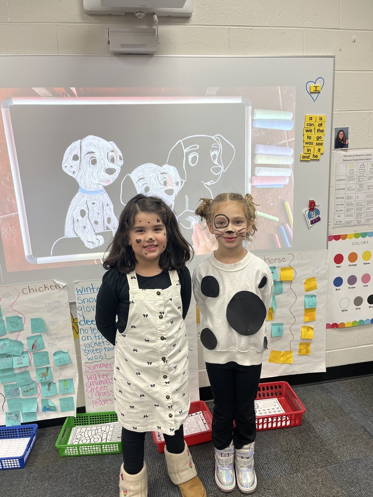 Two young girls in costume standing in a classroom with a white board behind them.