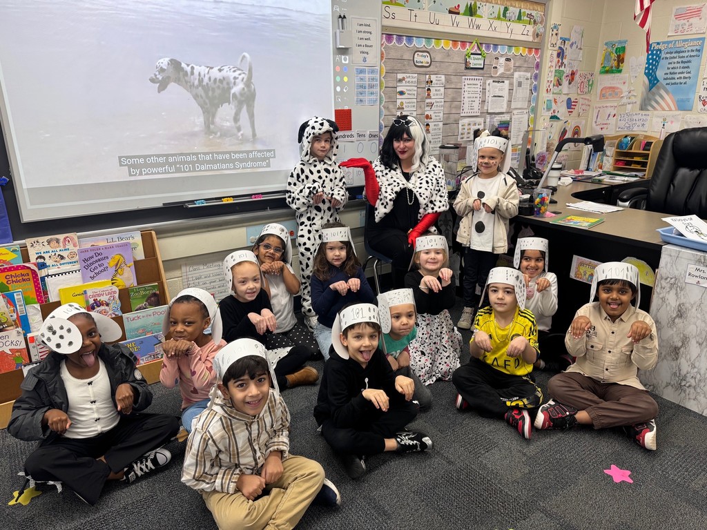 Classroom of young children in costumes posing for a photo with teacher, a screen in the background.