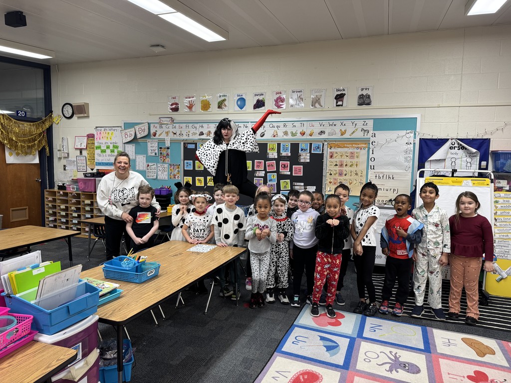 A group of children in pajamas poses for a photo with a performer in a classroom.