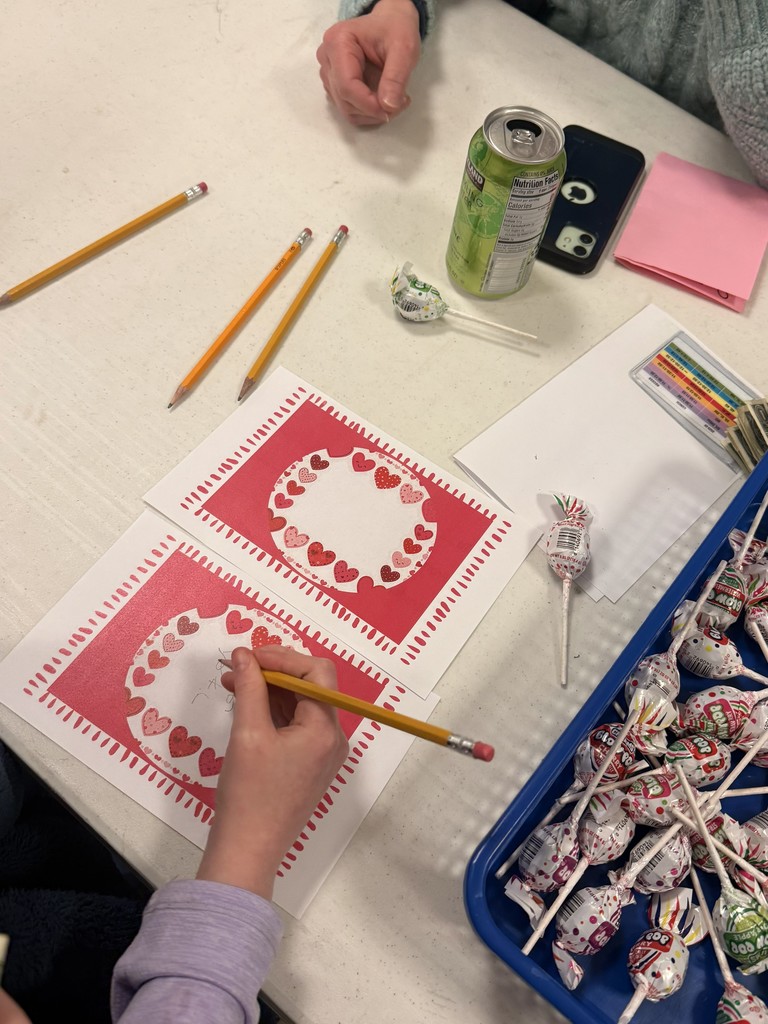 A person coloring a heart on paper. Pens, pencils, and lollipops are on a table.