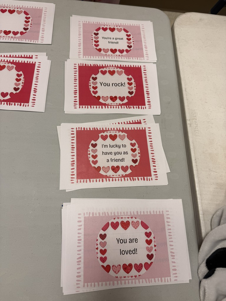 Multiple small cards with heart designs on a gray surface. Each card has a message. Background is plain gray.