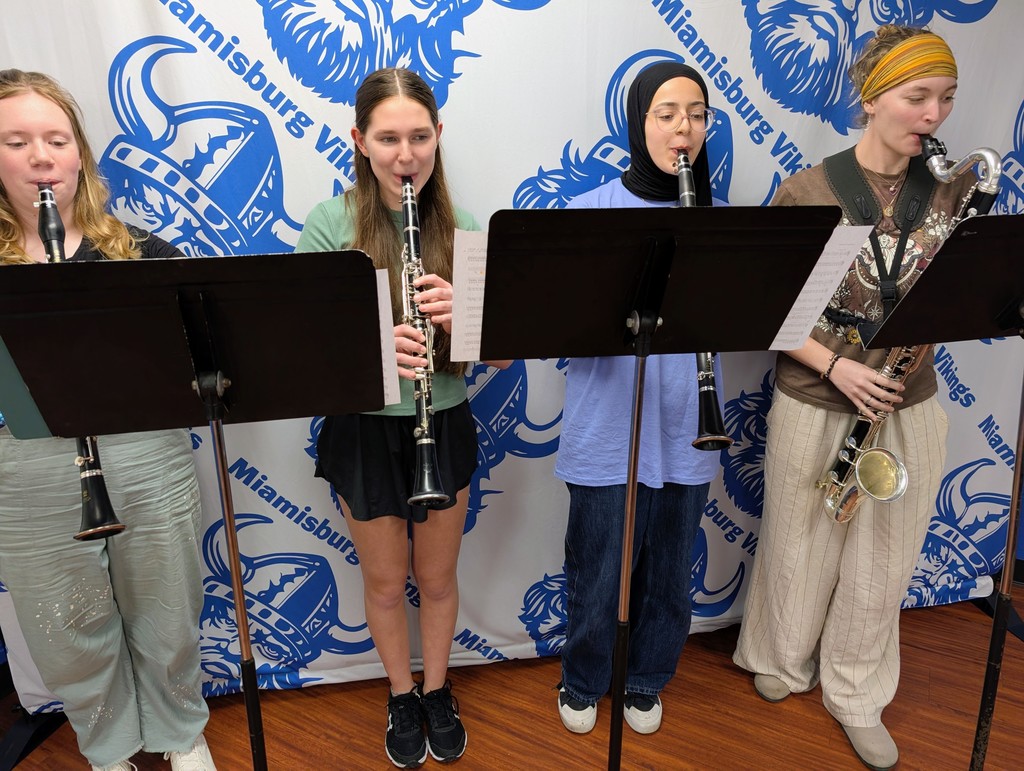Four students play clarinets while standing at music stands in front of a Miamisburg Vikings backdrop.