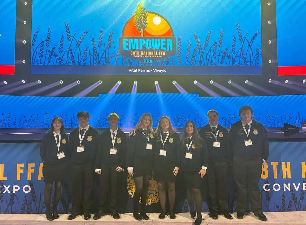 A group of individuals stand on stage wearing formal attire. A banner behind them reads "Empower" and "8th KFF Expo."