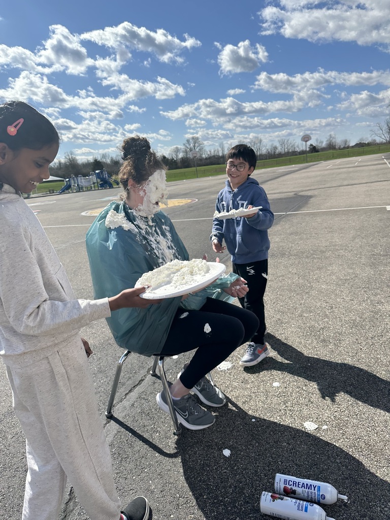 Three children, two holding plates of food, stand on a paved area with clear skies and scattered clouds.