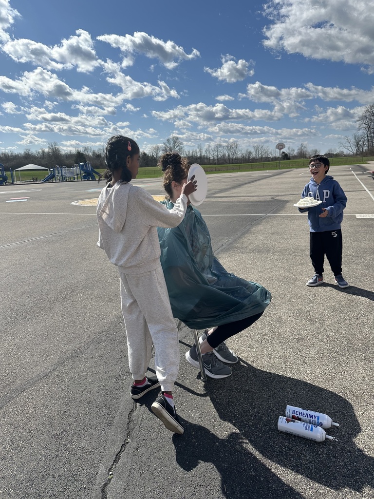 Three people in an open area. One person holds a plate, another sits in a chair, and one stands on a skateboard.