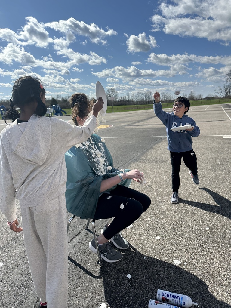 Three people on a runway, one person throws a paper plate at another person who is seated.
