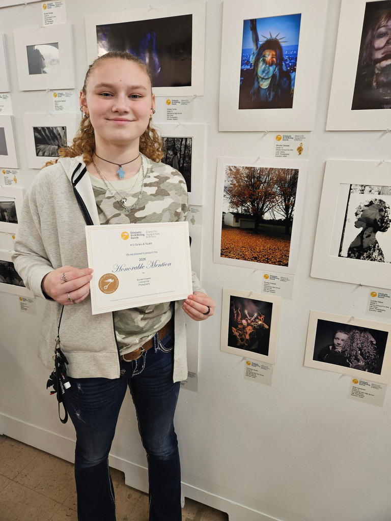 Person holding a certificate stands before a gallery wall filled with framed black-and-white photographs.