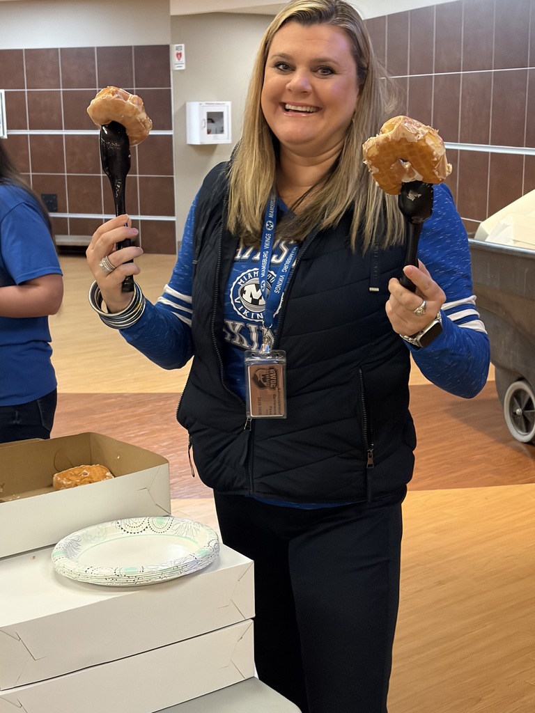 Woman holds two doughnuts on sticks in a room with a box of doughnuts and a plate.