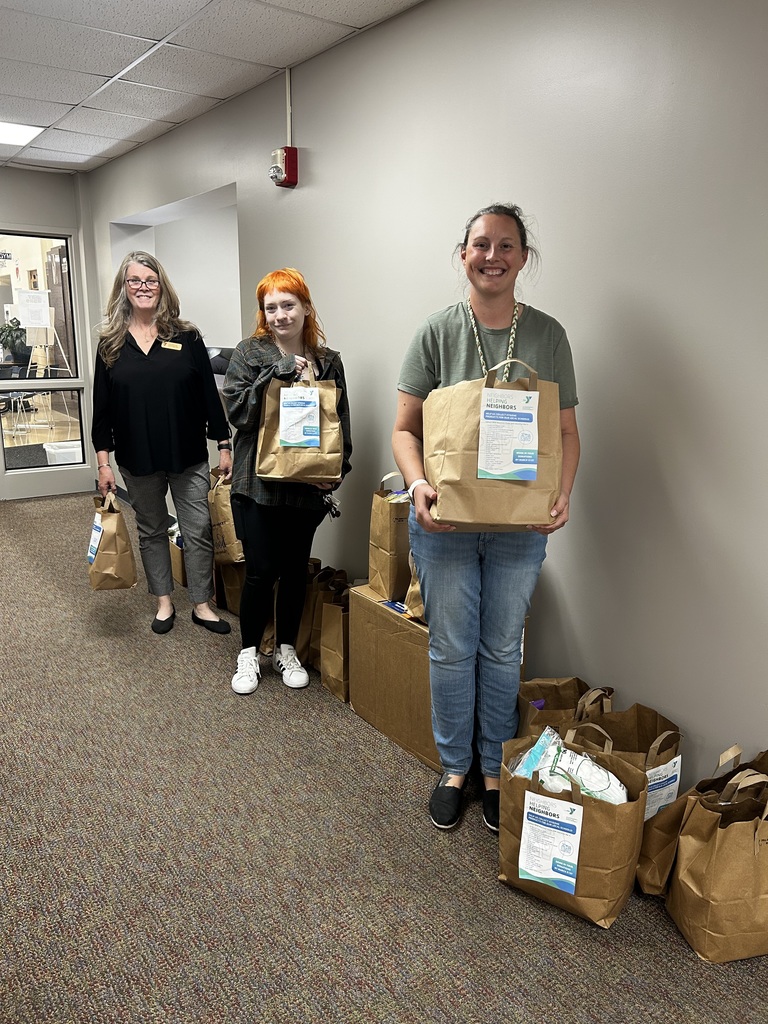 Three women in a corridor, one holding a bag, another with two bags, and a third with a bag and a box.
