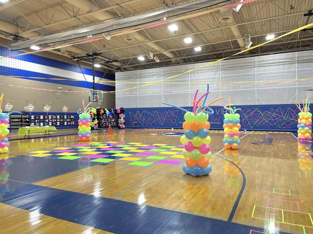 An indoor basketball court with a blue and white wall, colorful balloons, and a grid pattern on the floor.