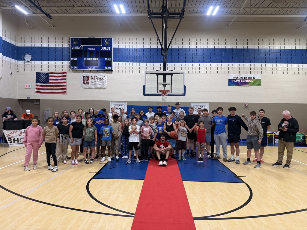 Indoor basketball court. People posing on a red carpet in front of a basketball hoop.