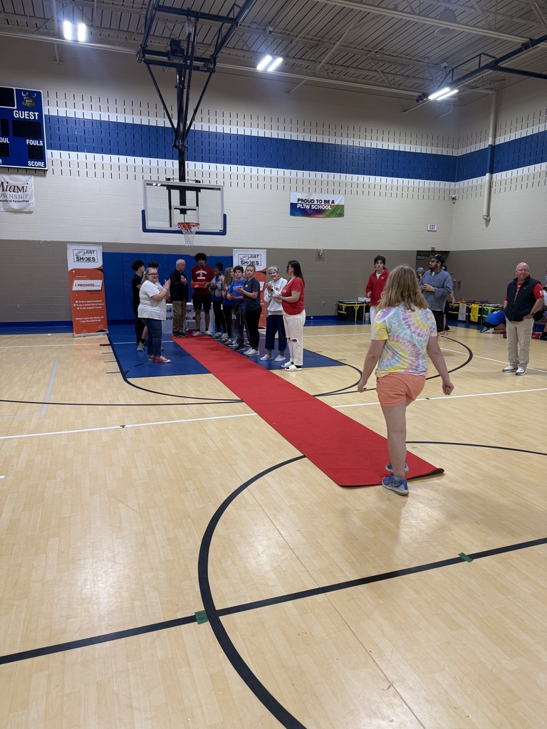 People in a gym walk across a red carpet. A basketball hoop is on the wall.