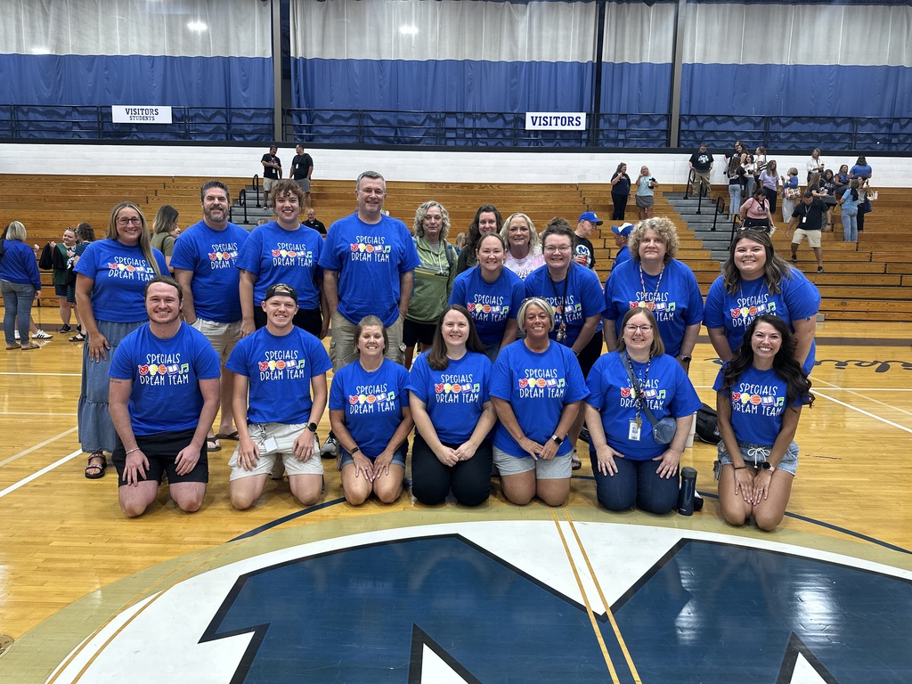 A group of people in blue shirts posing on a basketball court with a large "W" logo.