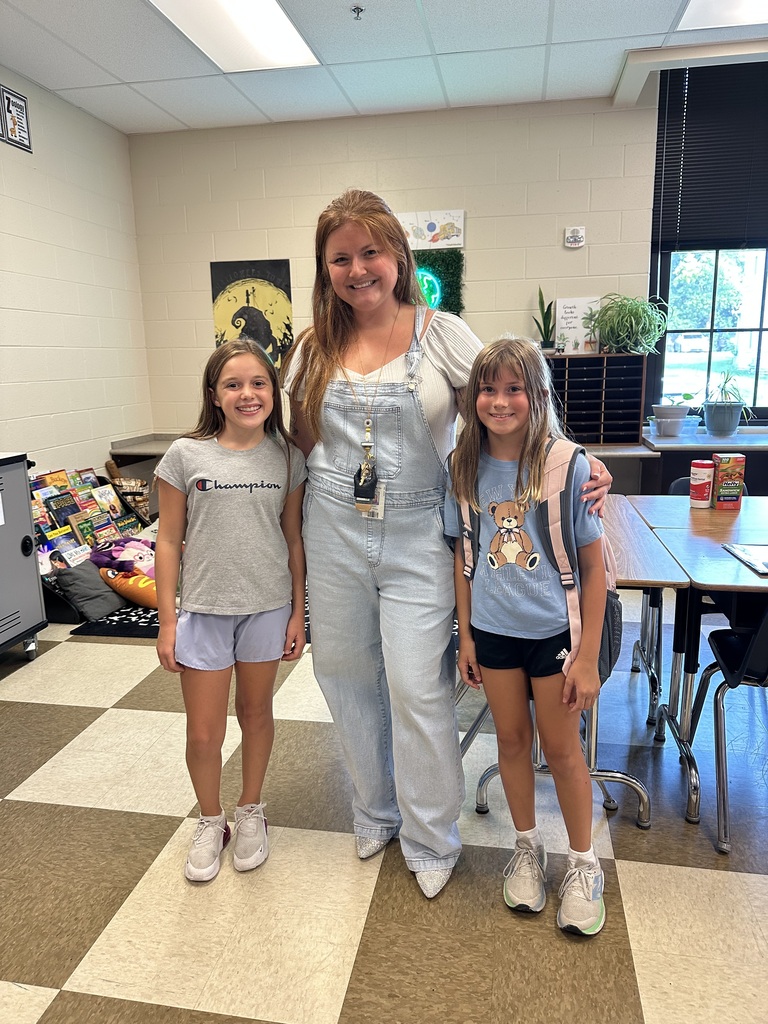 Woman and two girls in school hallway. The woman is in overalls and the girls are in T-shirts.
