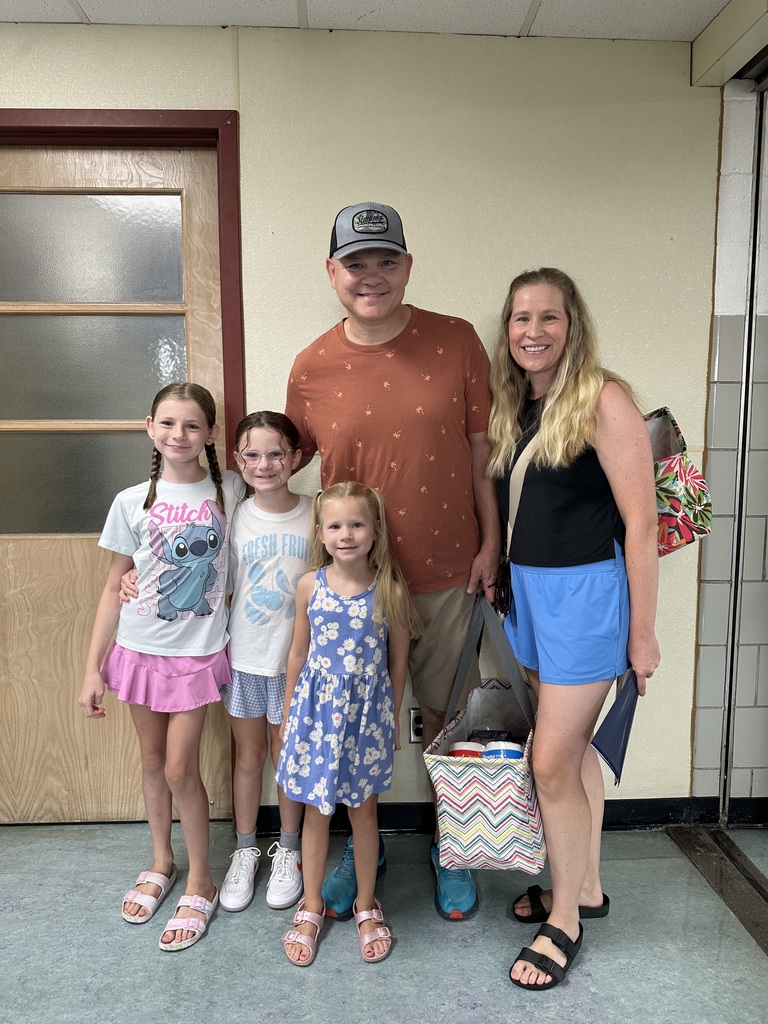 A man and four children stand together in front of a door; three girls wear dresses and sandals.