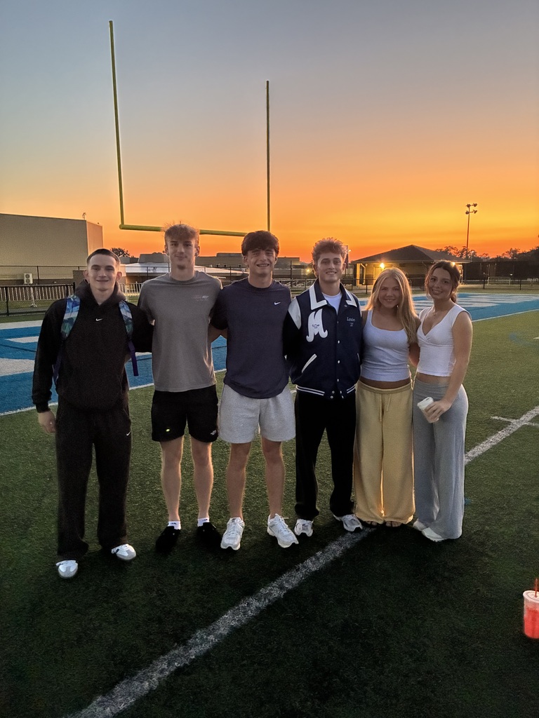 Six people pose together on a football field as the sun sets in the background.