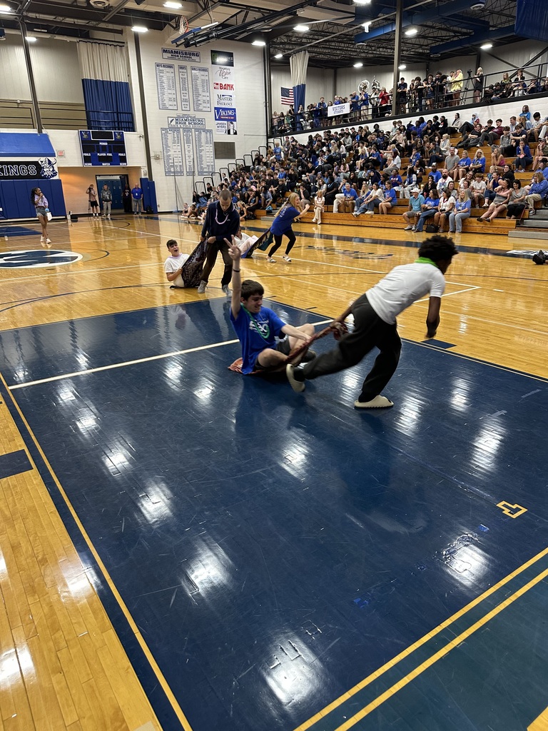 Several individuals on a basketball court engage in a game, with a player attempting to tackle another. Spectators watch from the stands.