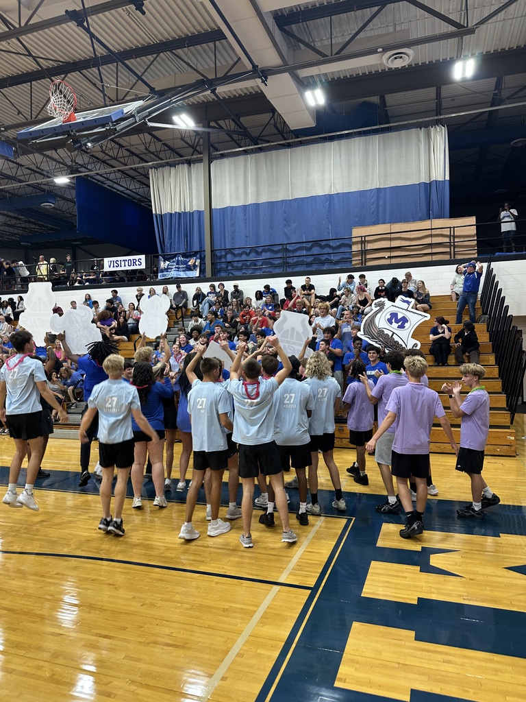 Group of people wearing matching shirts, standing in a circle on a basketball court. Some are holding signs.