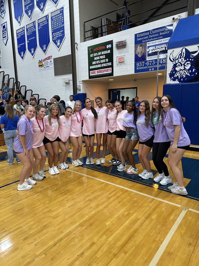 Group of girls in pink shirts and black shorts standing on a basketball court, posing for a photo.