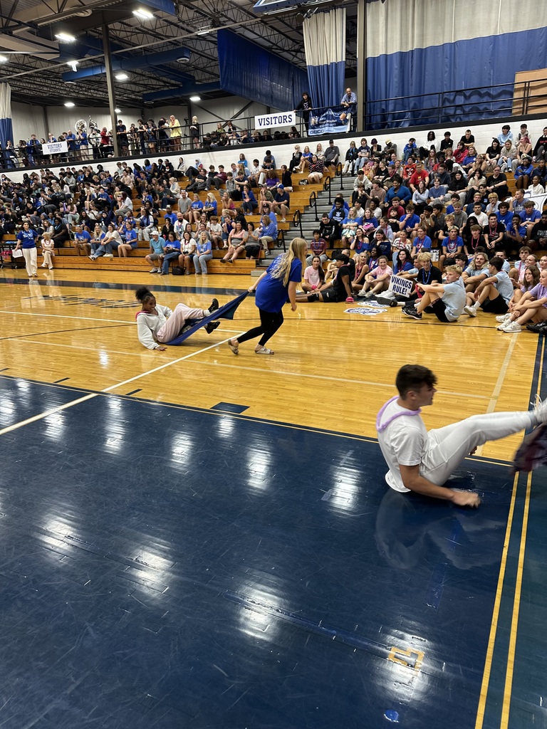 Three individuals engage in a floor exercise on a basketball court with a crowd of spectators.
