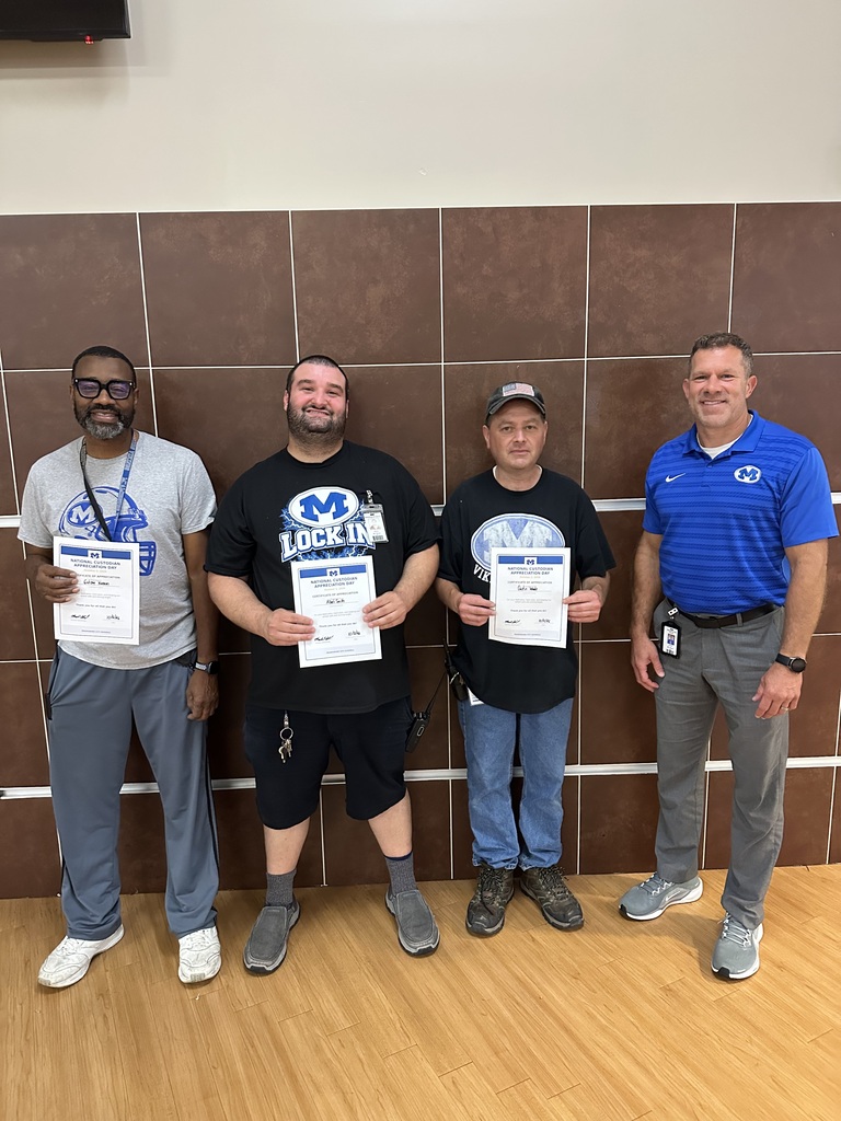Four adult males stand in a row holding certificates. A brown wall is behind them.