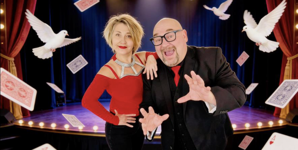 Man and woman in front of a stage with doves and cards flying around them
