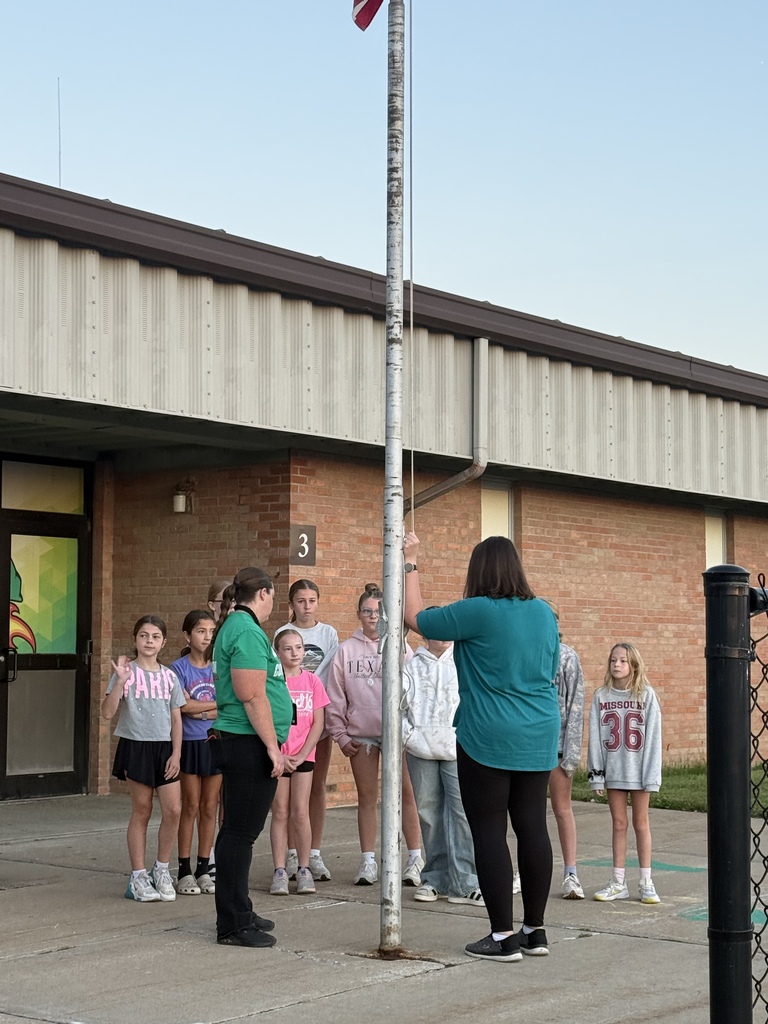 Students and STUCO representatives gather around a flag pole outside of a school