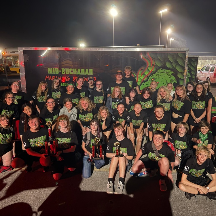 students in black t-shirt in front of an enclosed trailer with three trophies