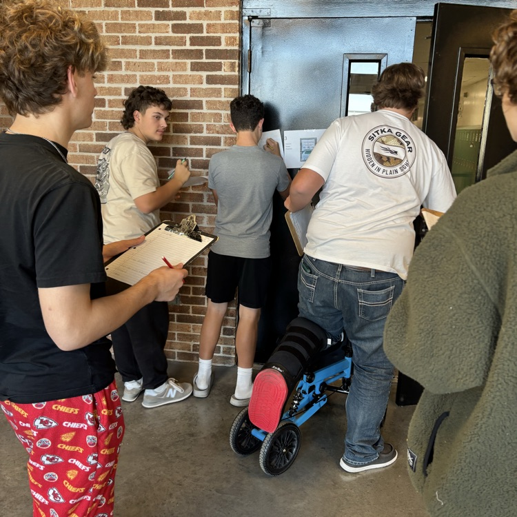 5 boys analyzing a picture taped to a brick wall