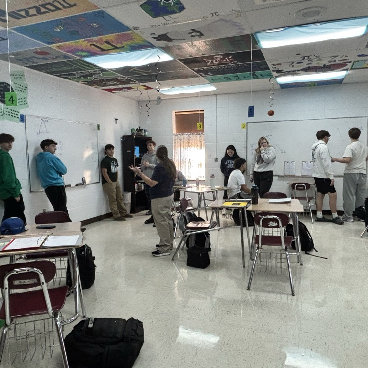 multiple students writing on white boards around a classroom