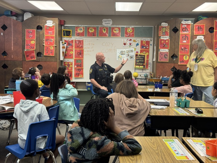 1st grade students sitting on the carpet, listening to a police officer read a book