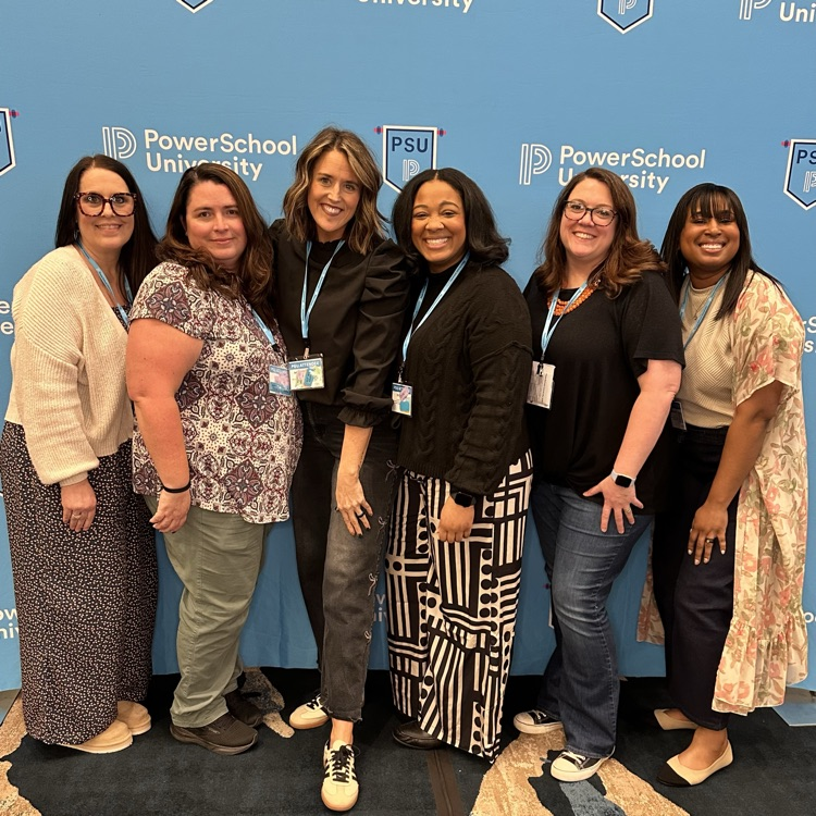 A team from Mid-Del attended PowerSchool University training. They are pictured in front of an event backdrop. 