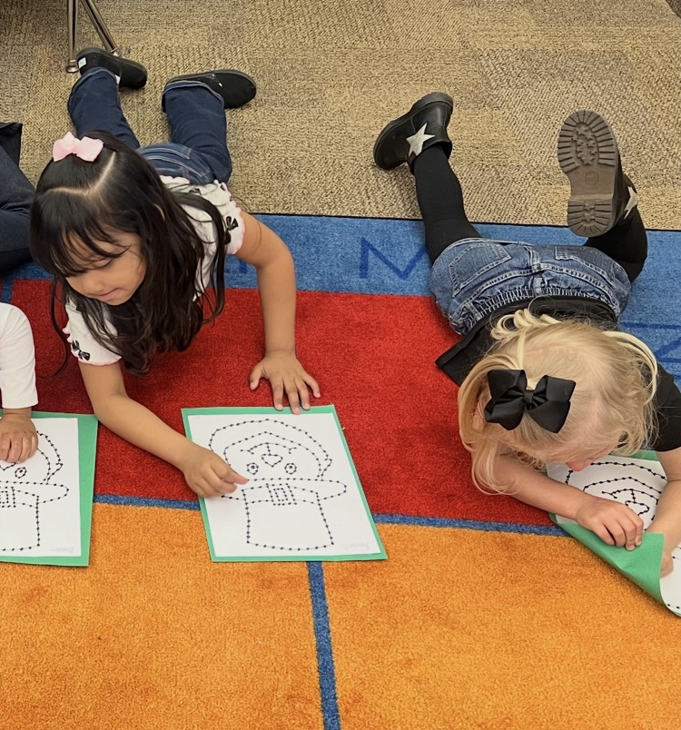 pre-K students on the carpet doing a fine motor activity. The activity is a punch and poke leprechaun for St. Patrick’s Day. 