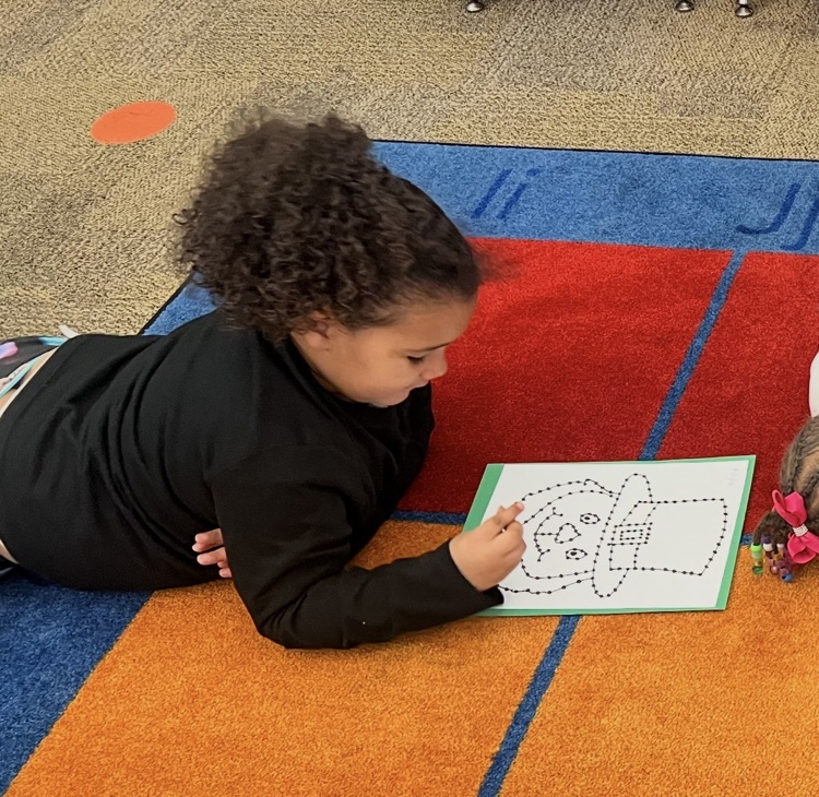  pre-K students on the carpet doing a fine motor activity. The activity is a punch and poke leprechaun for St. Patrick’s Day