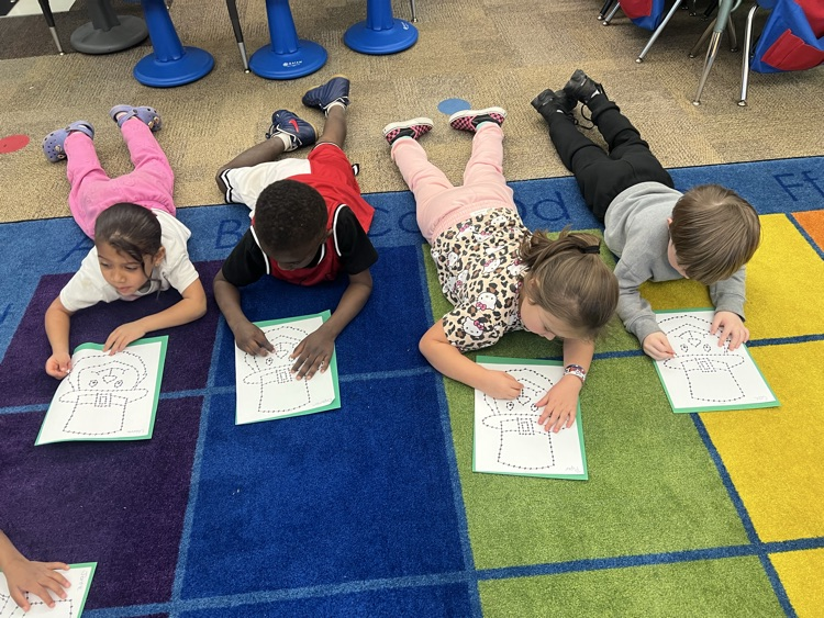  pre-K students on the carpet doing a fine motor activity. The activity is a punch and poke leprechaun for St. Patrick’s Day