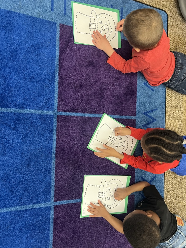 pre-K students on the carpet doing a fine motor activity. The activity is a punch and poke leprechaun for St. Patrick’s Day
