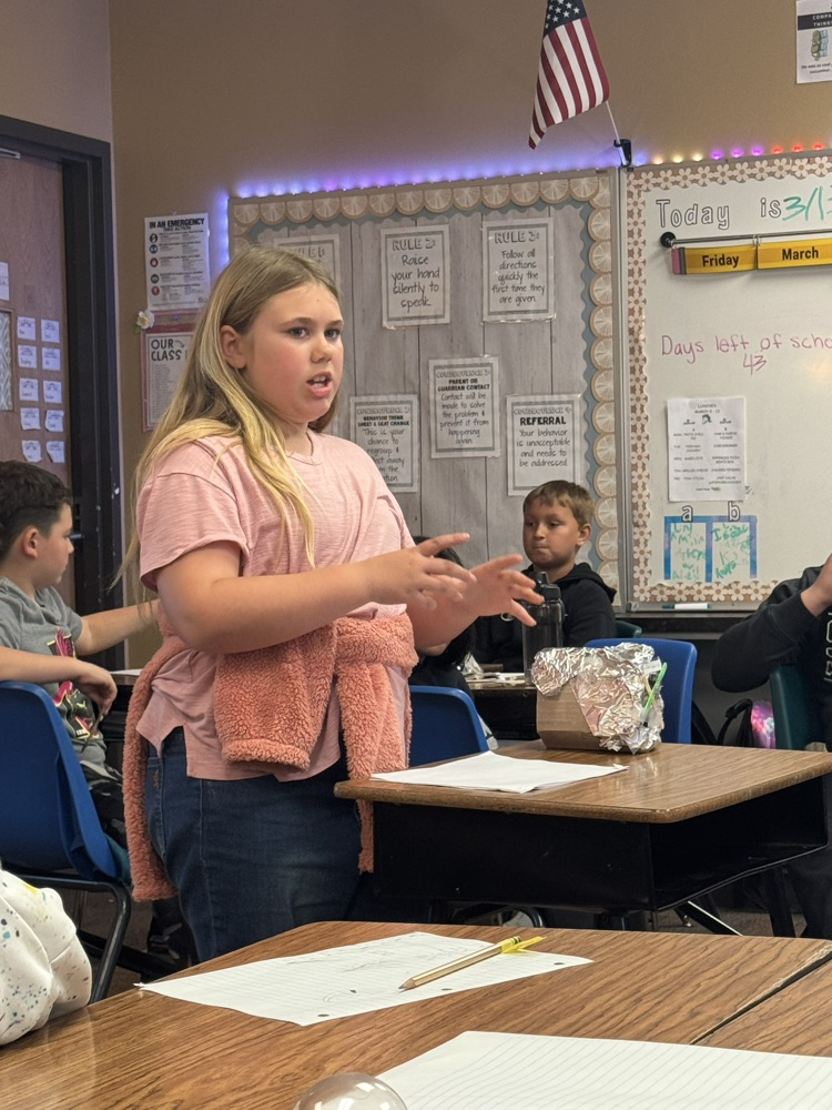 leprechaun traps made by fourth graders. The students are in front of the room, presenting them.