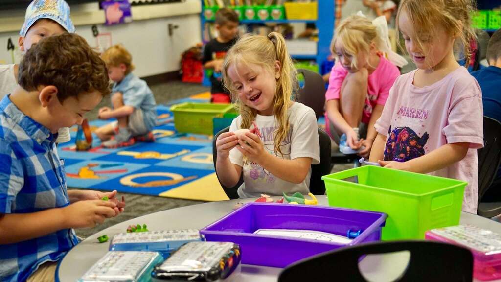 Several children in a classroom, one girl smiling while looking at a small object.