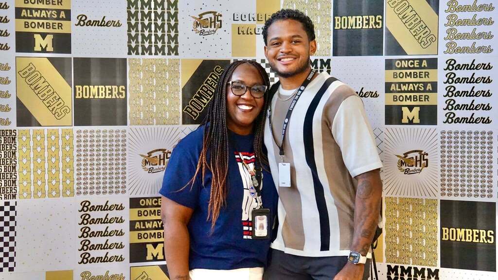 Two people standing next to each other in front of a colorful collage with "BOMBERS" and "M" designs.