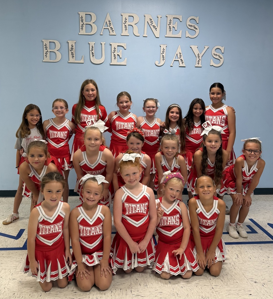 A group of young girls in red cheerleading uniforms pose for a photo in front of a wall.