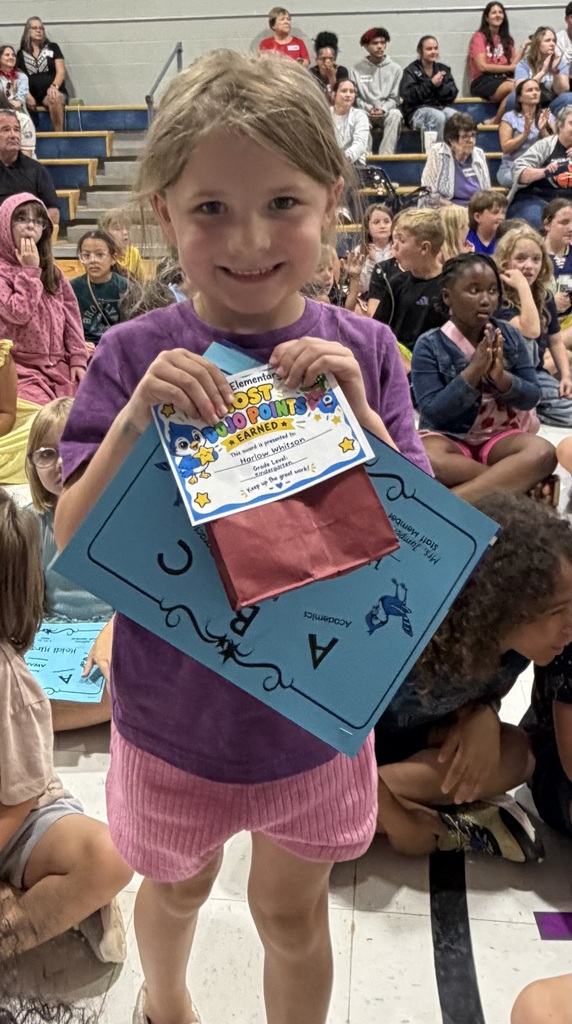 Girl in purple shirt holding a certificate and a red bag on top.