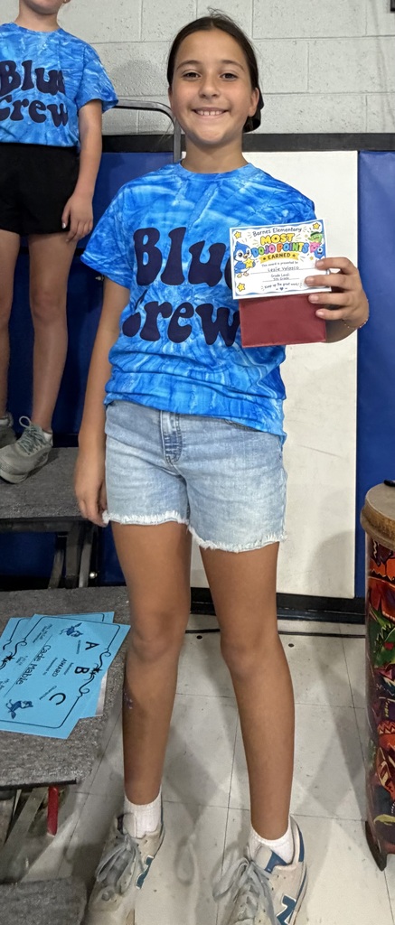 A girl wearing a blue tie-dye t-shirt and denim shorts holds a certificate.