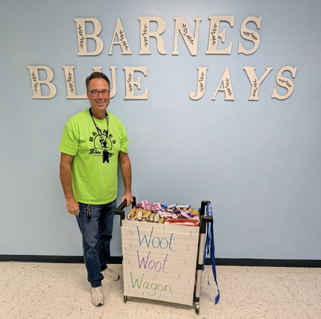 Mr. Becker stands next to a cart with snacks on it in front of a Barnes Blue Jays sign.