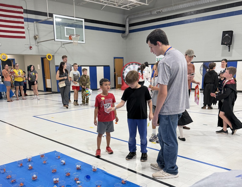 A group of children and adults in a gymnasium, one man giving instructions to two boys.