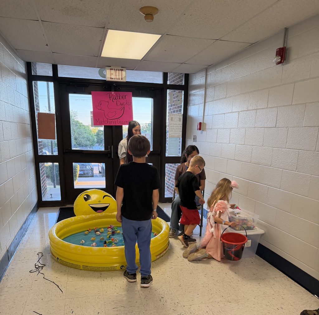 Group of children in a hallway. Some standing and others seated near a small pool.