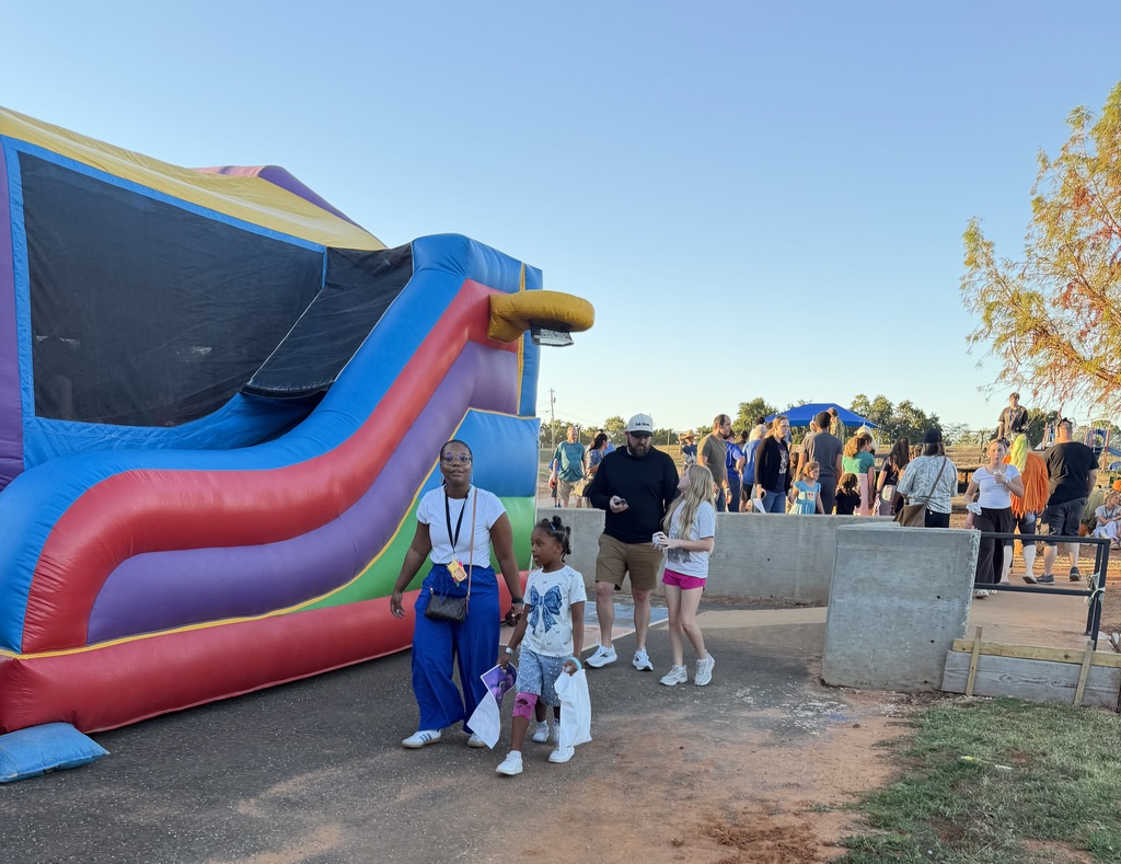 A large colorful inflatable slide stands on an outdoor area with people walking by. Some hold bags.