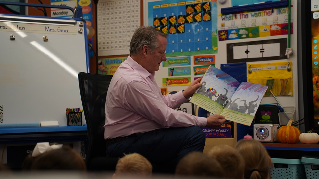 A man sits in a chair holding a book while reading to a group of children.
