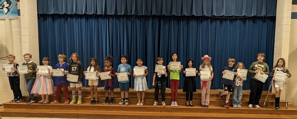 Group of young students holding certificates with a blue curtain in the background.