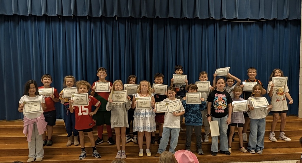 A group of students on a stage holding white certificates in front of a blue curtain.