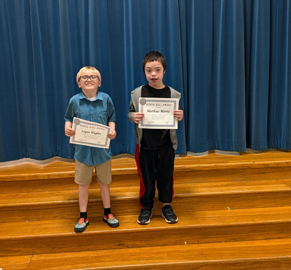 Two students stand on a stage, holding certificates, with a blue curtain in the background.